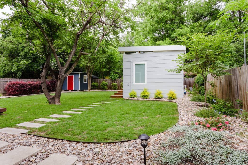 Backyard with two small sheds and a stone pathway through the grass, trees surround.