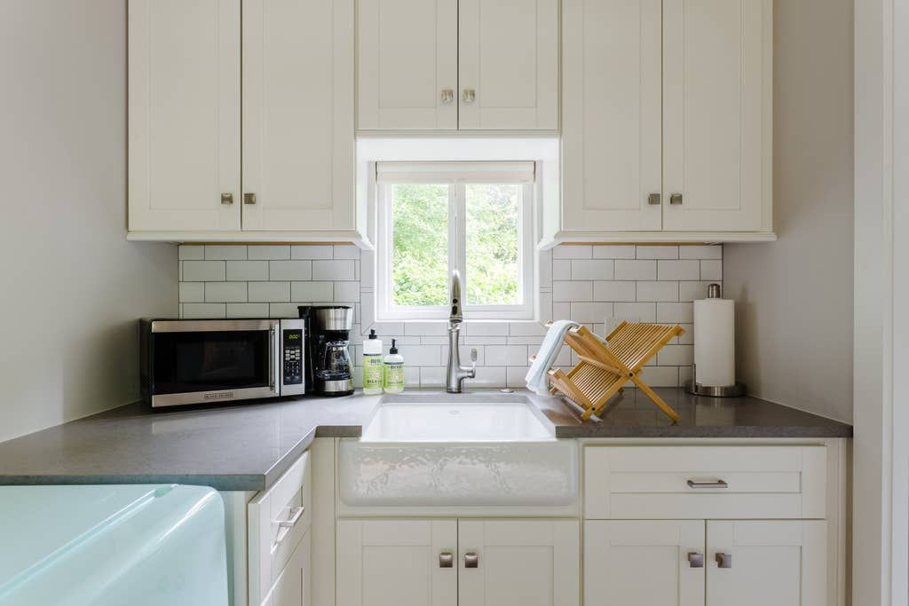 White kitchen with cabinets, sink, window, appliances, and countertops.