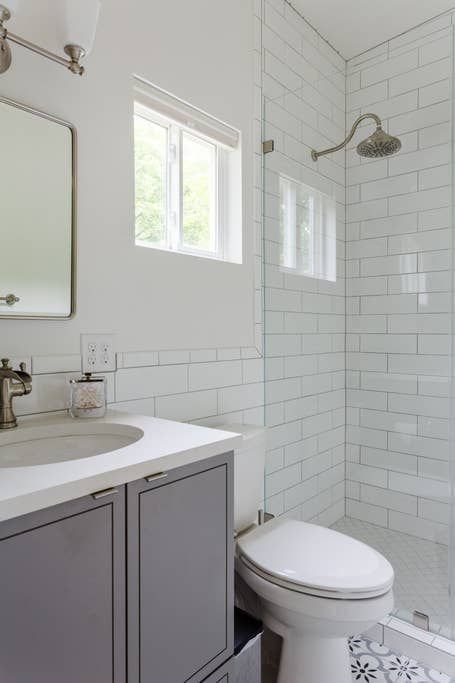 Gray and white bathroom with shower, toilet, sink, and window.