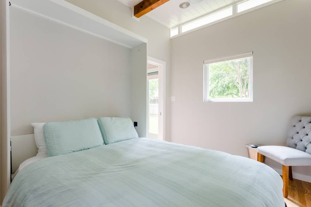 Bedroom with bed, pillows, chair, window, and wood beam. Pale blue and white color scheme.