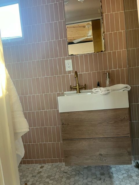Bathroom with pink vertical tiles, wooden vanity, gold faucet, mirror, and hexagon floor tiles.