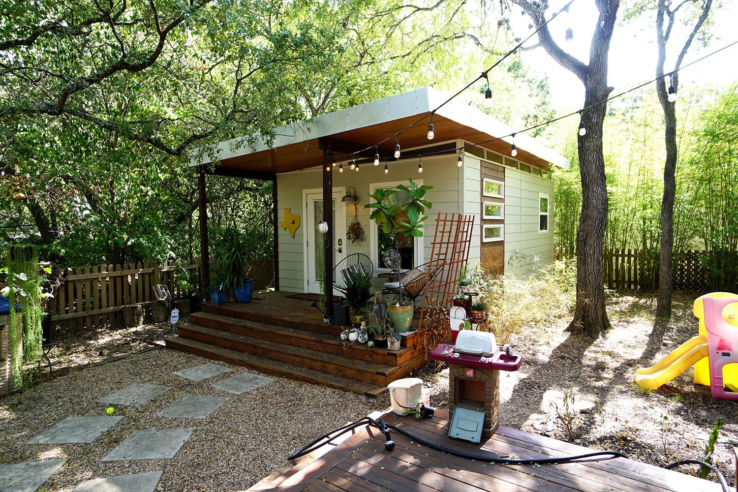 A small house with a porch and a slide in the backyard surrounded by trees.