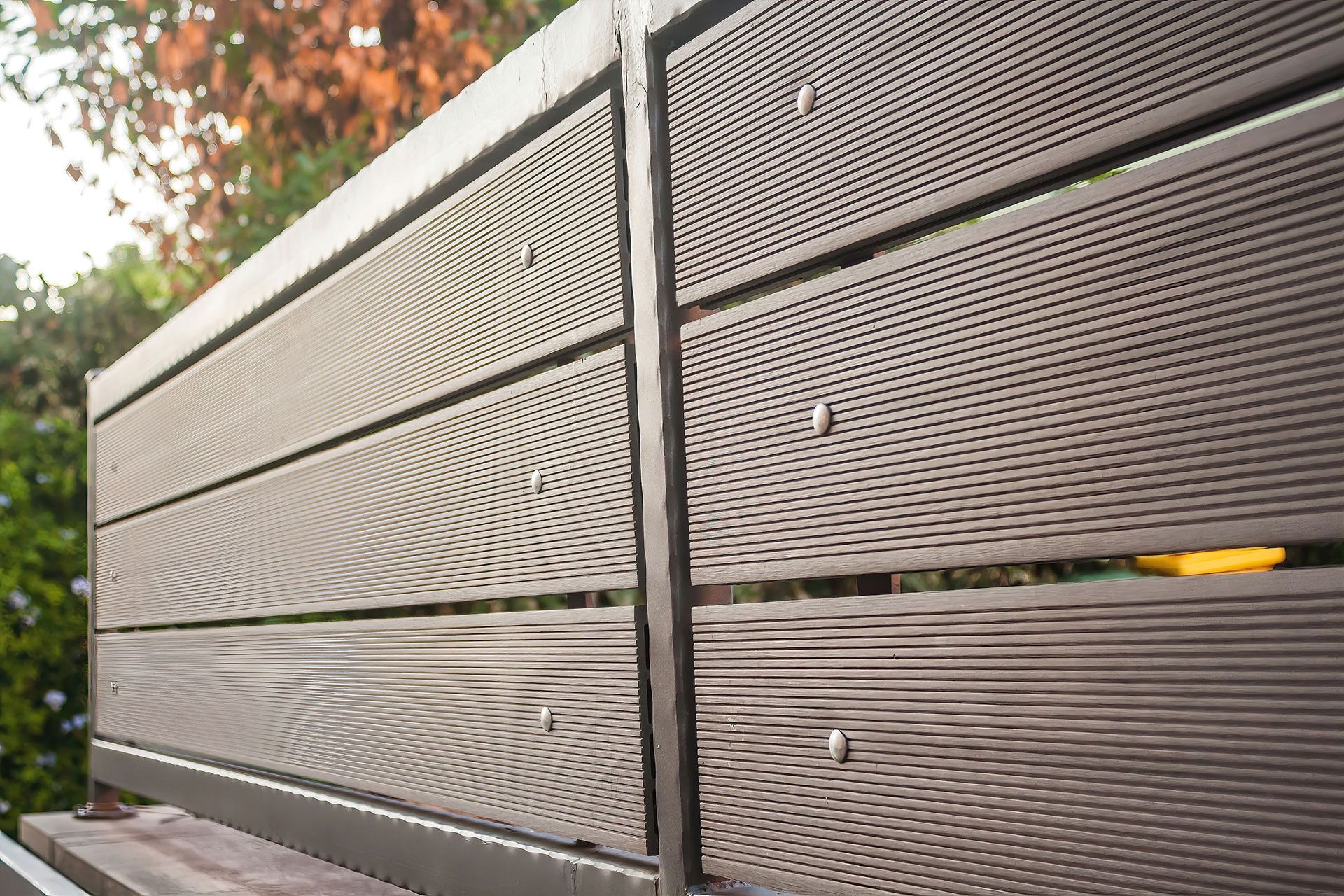 Brown and gray horizontal slat fence in a garden setting, secured with silver fasteners.