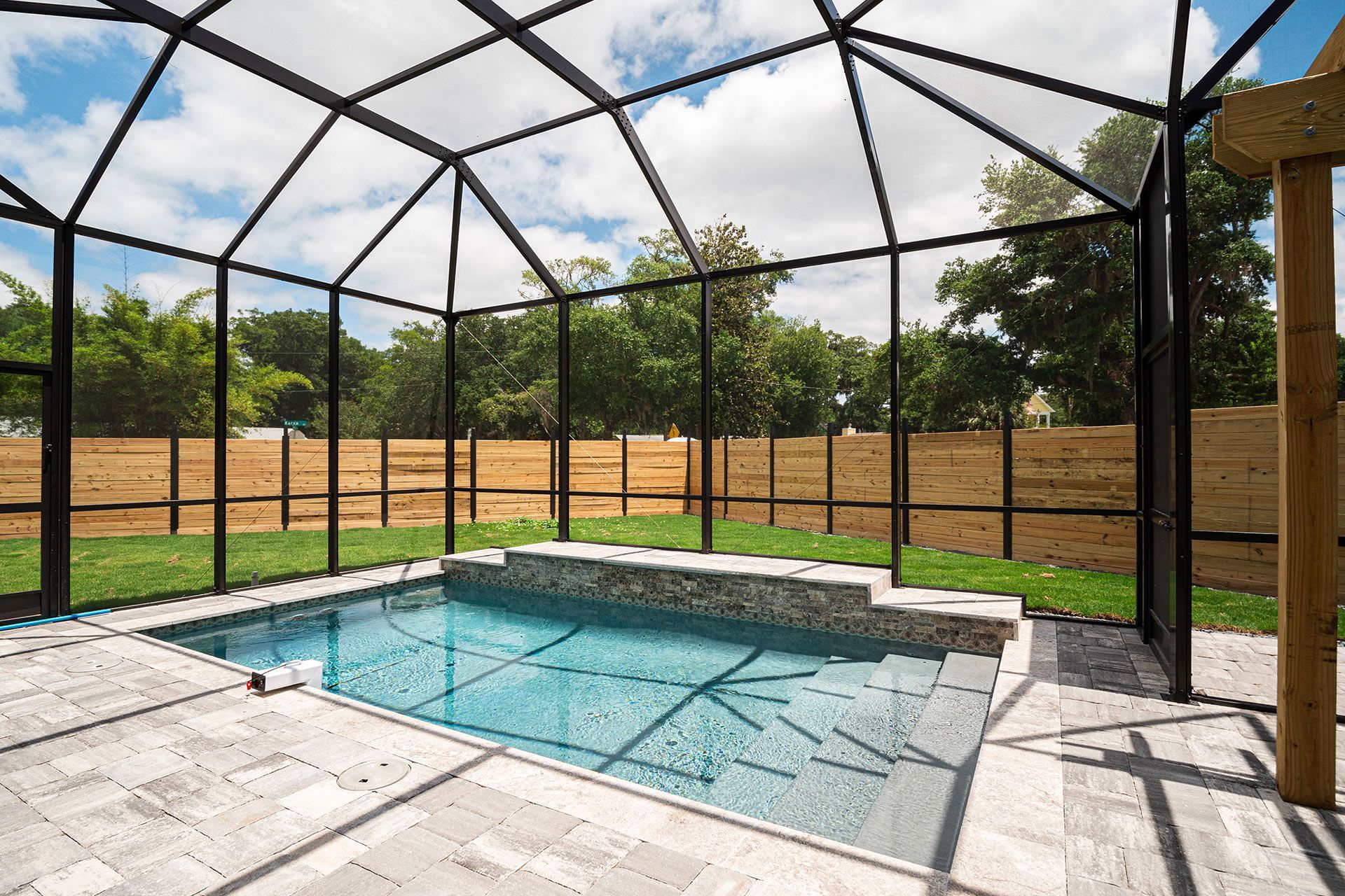 Pool enclosure with small pool and stone steps, surrounded by a black frame and greenery.