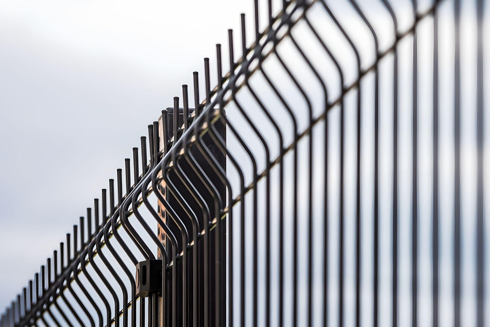 Close-up of a black metal security fence with a wavy design against a light sky.
