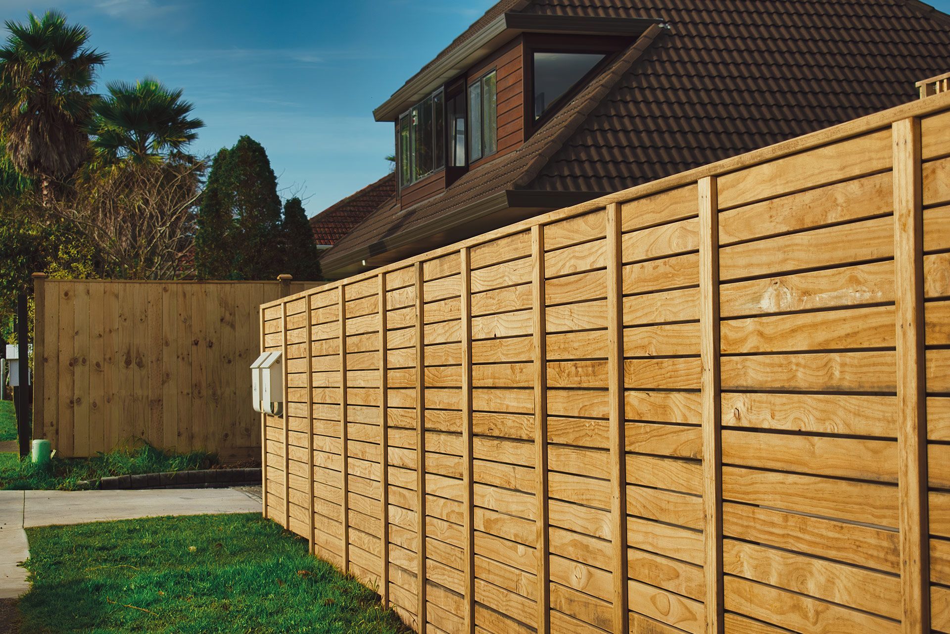 Wooden fence in front of a house, green grass, and blue sky.