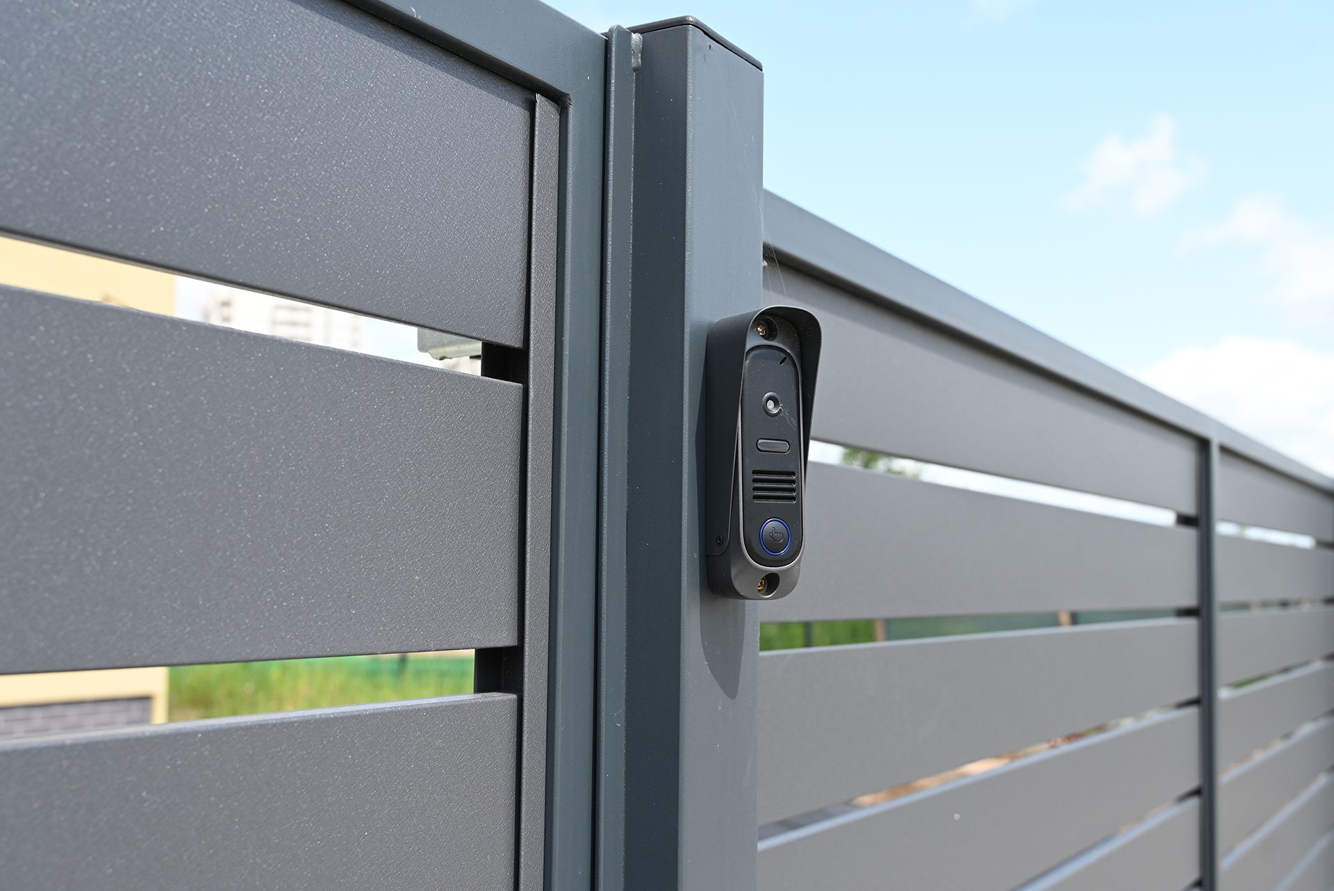 A gray metal gate with an intercom system mounted on a post.