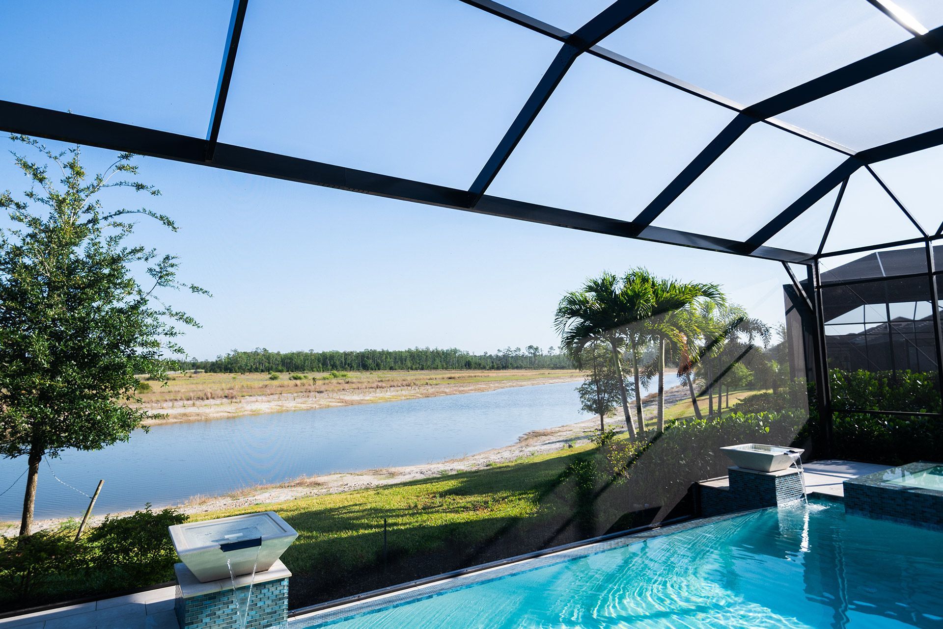 Pool overlooking a river and landscape framed by a screened enclosure on a sunny day.
