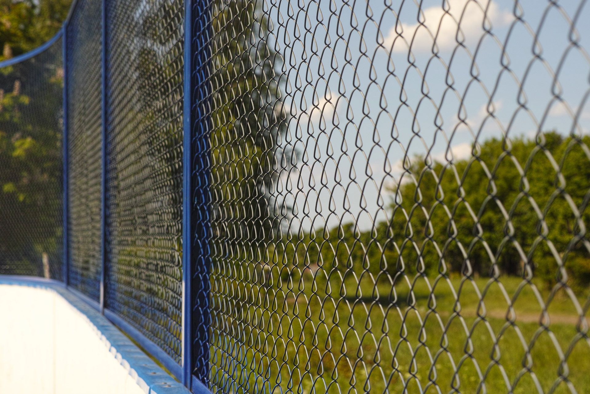 Black metal fence bordering a grassy area with trees and a building in the background.