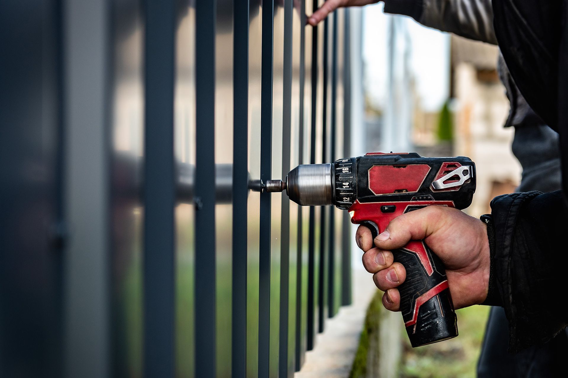 Person using a red and black drill to attach a metal fence.
