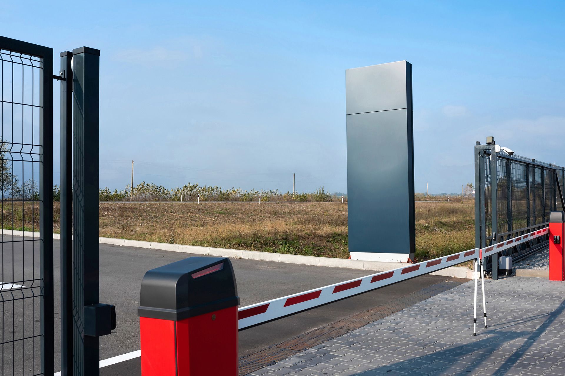 Black metal fence bordering a grassy area with trees and a building in the background.
