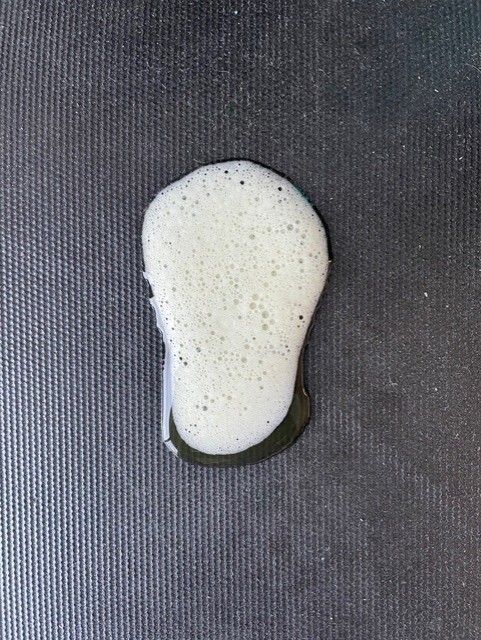 White, foamy substance spilled on a textured, dark gray surface. White, foamy substance spilled on a textured, dark gray surface.