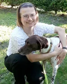 A woman is kneeling down next to a brown and white dog.