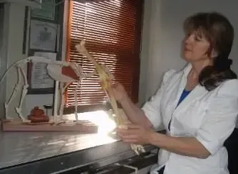 A woman in a lab coat is holding a model of a dog 's skeleton.
