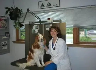 A woman in a lab coat is sitting next to a dog