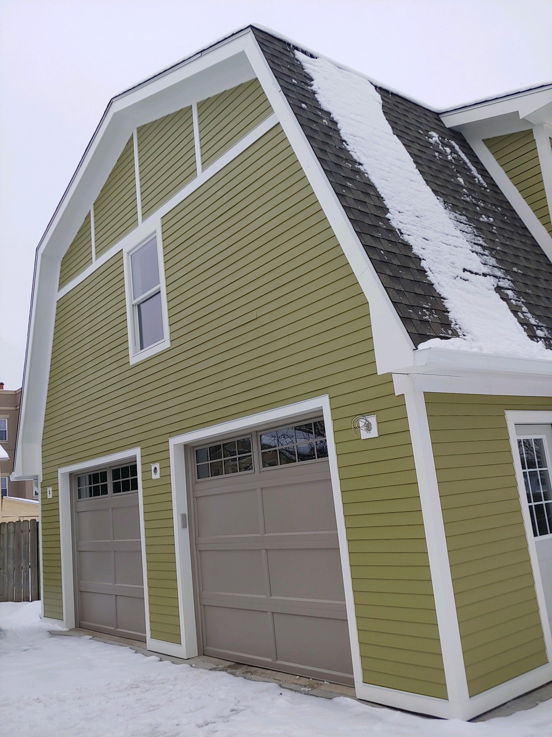 A green house with two garage doors and a snowy roof