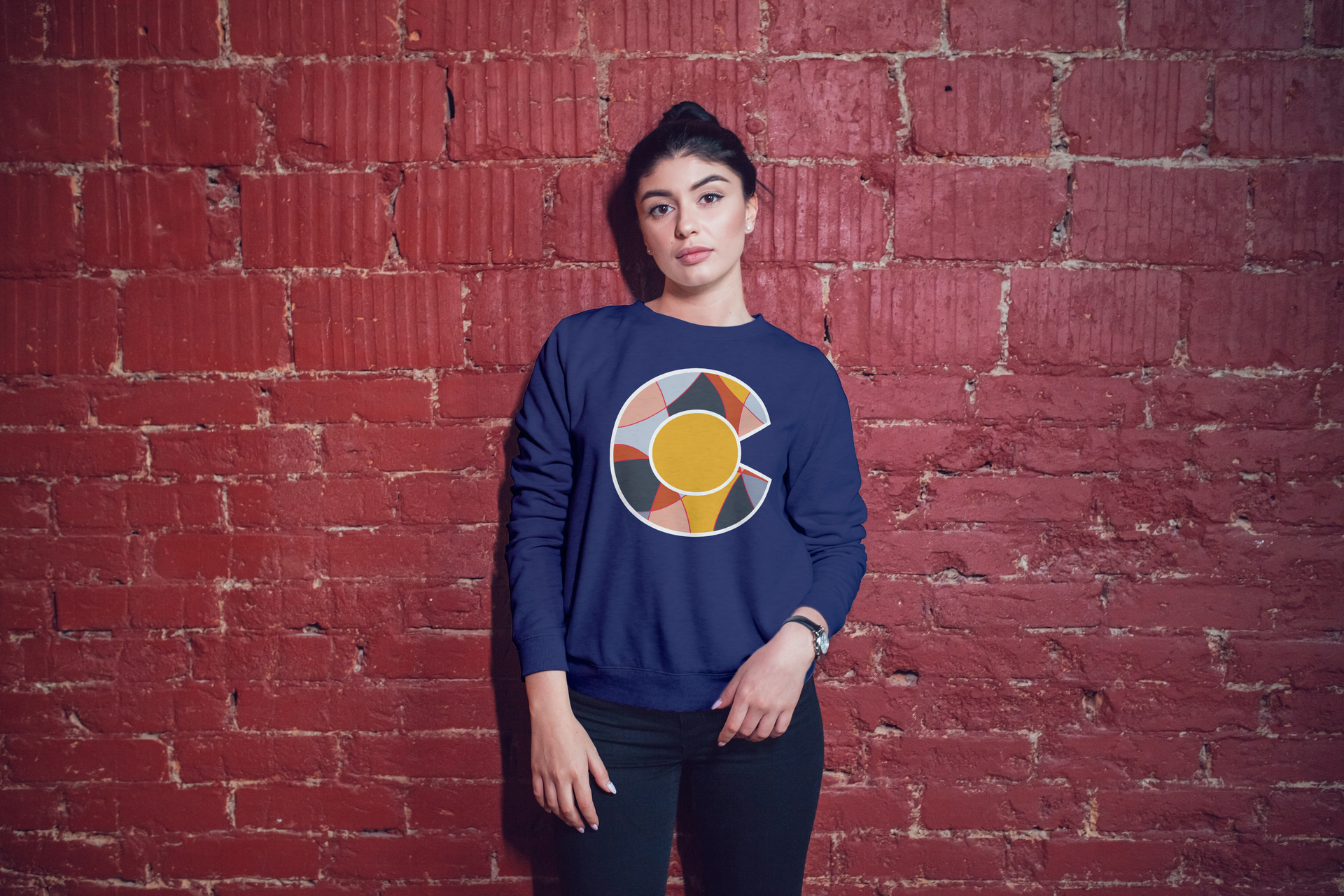 young woman wearing graphic Colorado long sleeve tee standing in front of red brick wall