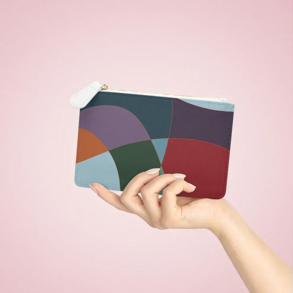 light skinned hand holding small clutch purse with gem tone graphic artwork and white zipper in front of pink background