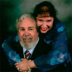 Woman hugging a man, both smiling. They are in front of a teal background.