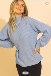 A woman is wearing a light blue sweater and black pants.