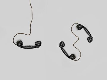 Two old fashioned telephones hanging from a wire on a white background