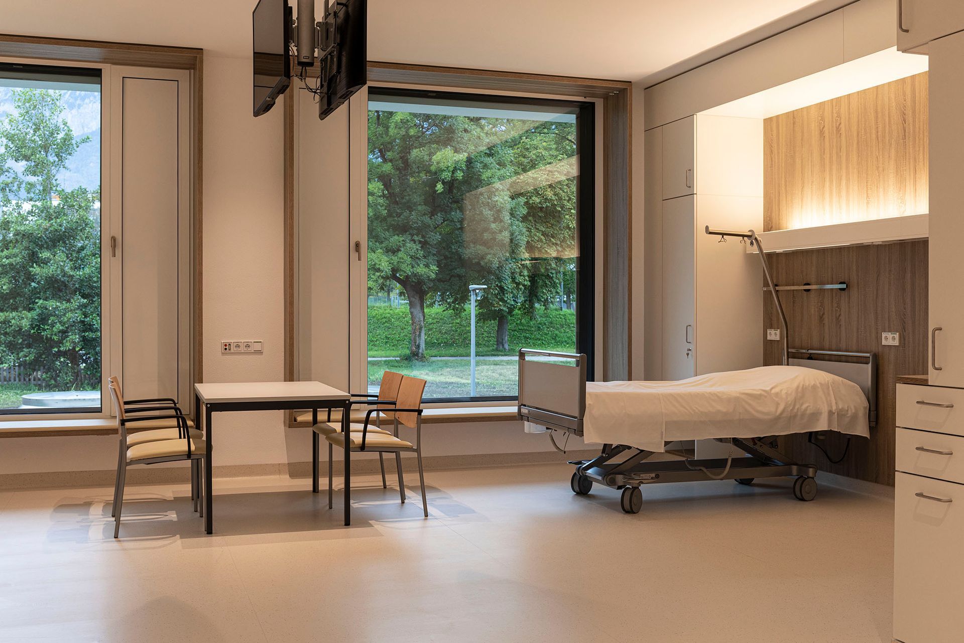 Ein Krankenhauszimmer mit Bett, Tisch und Stühlen.