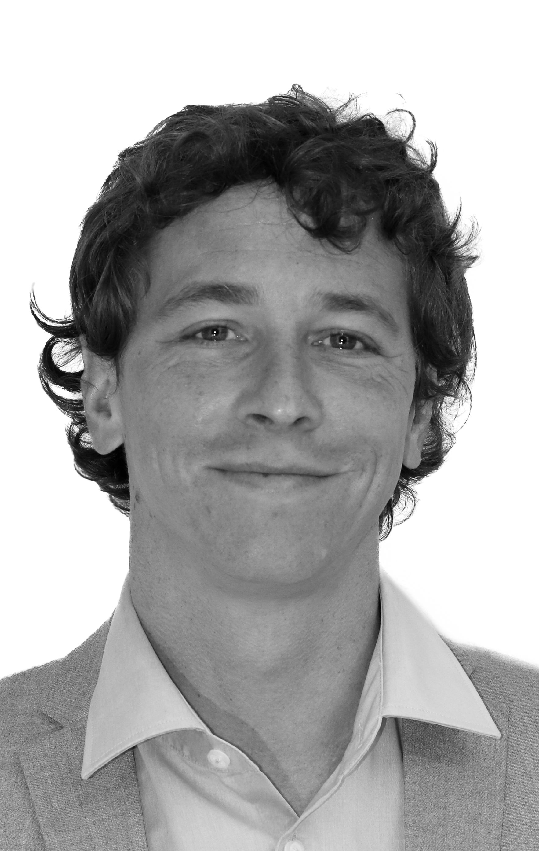 Ein Mann mit lockigem Haar lächelt auf einem Schwarzweißfoto.