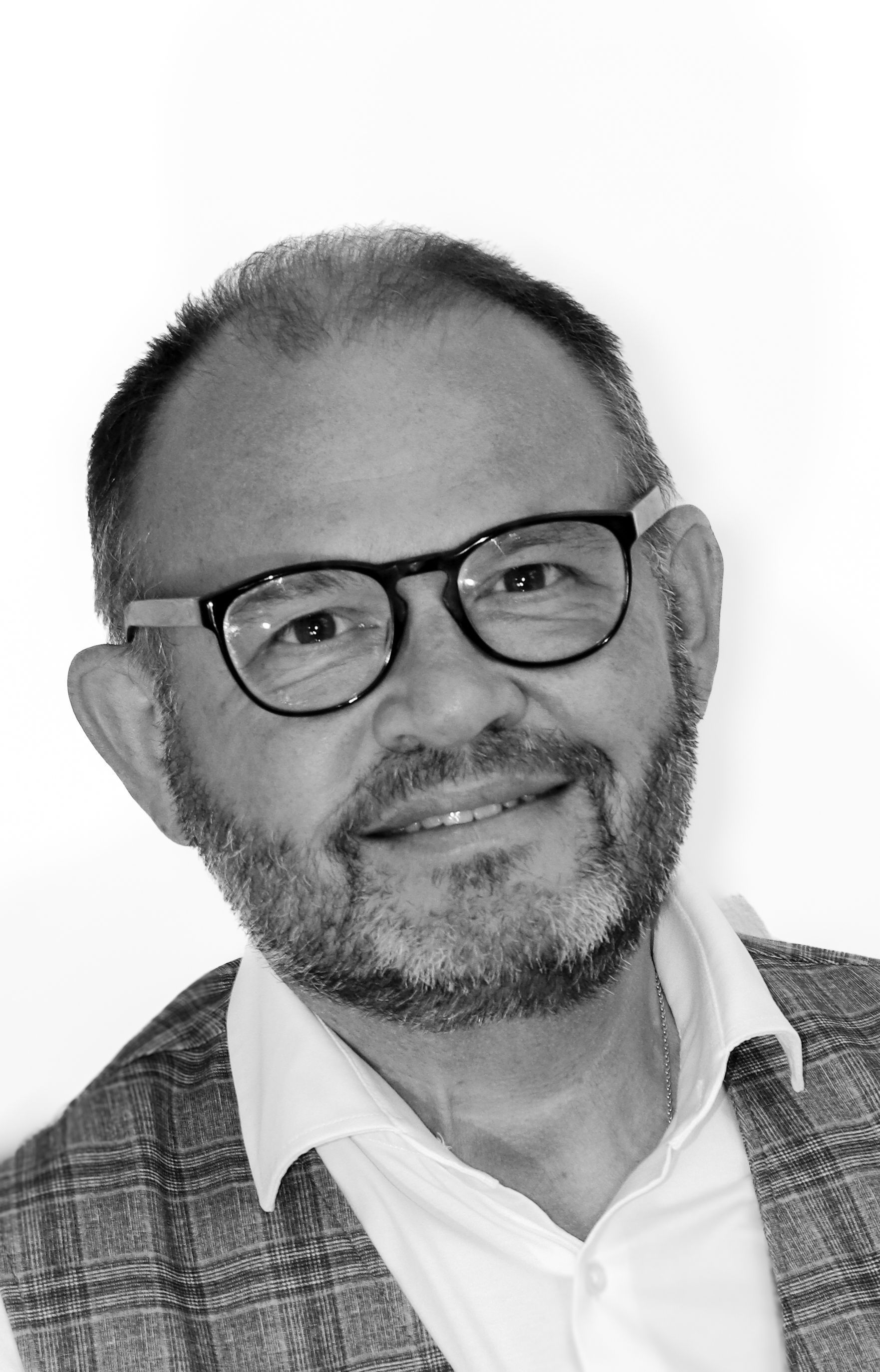 Ein Mann mit Brille und Bart lächelt auf einem Schwarzweißfoto.