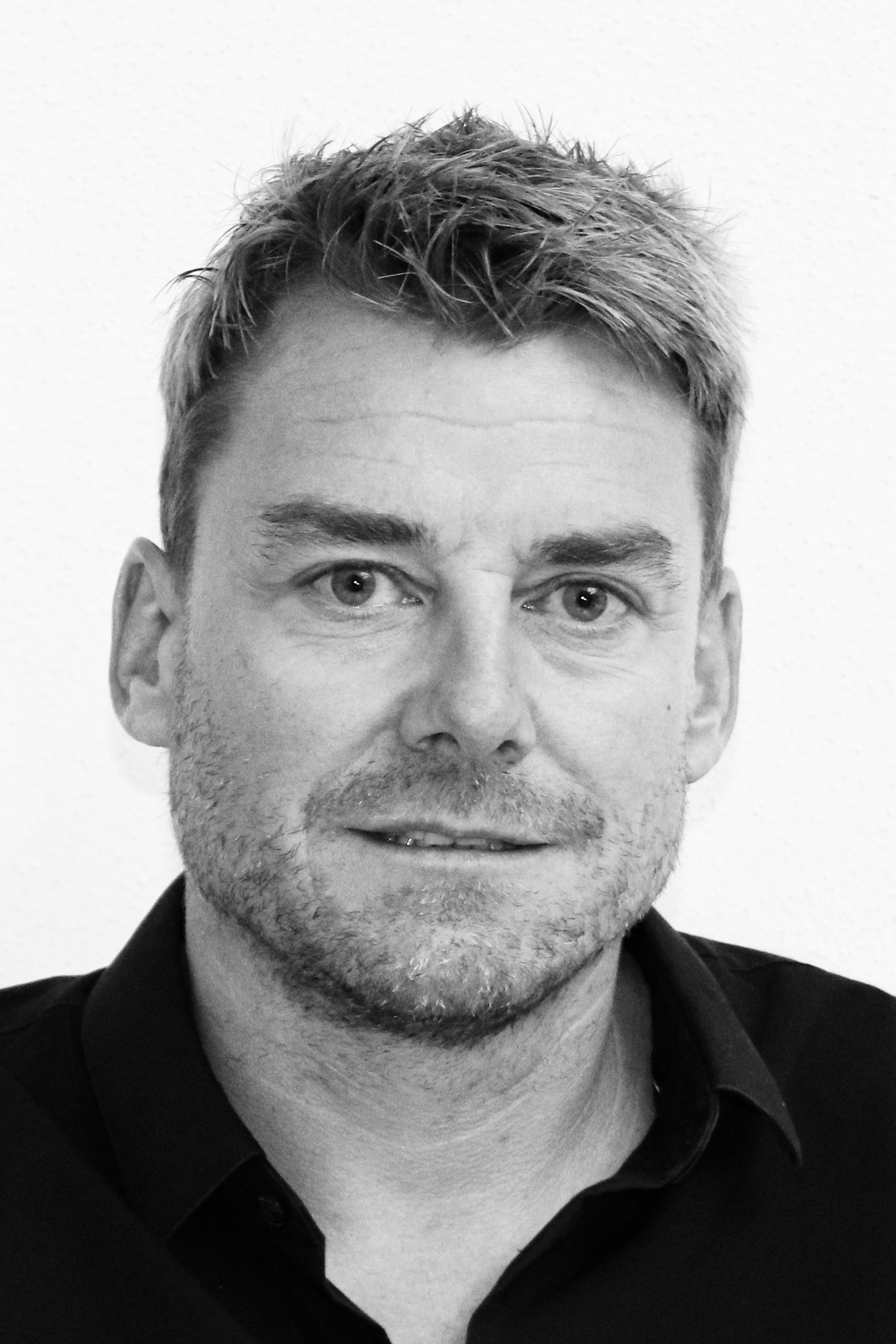 Ein Schwarzweißfoto eines Mannes mit Bart, der ein gestreiftes Hemd trägt.