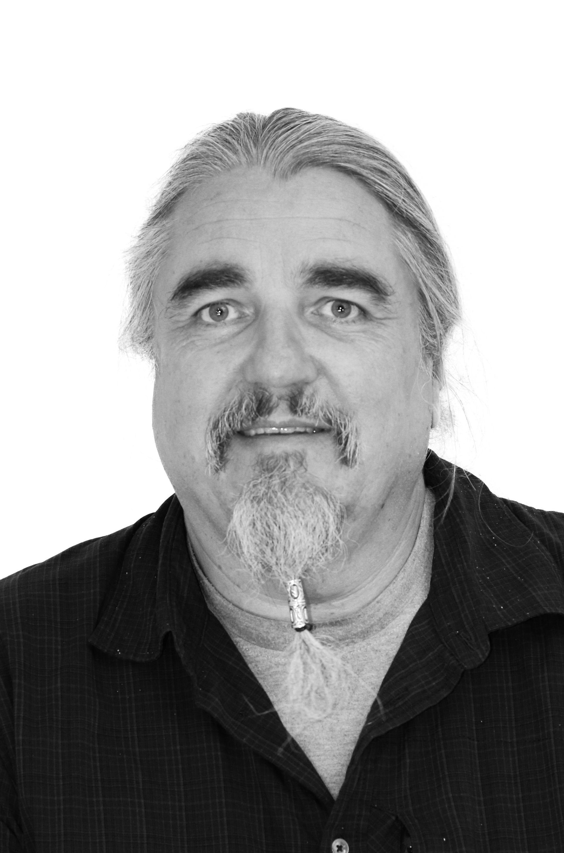 Ein Mann mit langen Haaren und Bart lächelt auf einem Schwarzweißfoto.