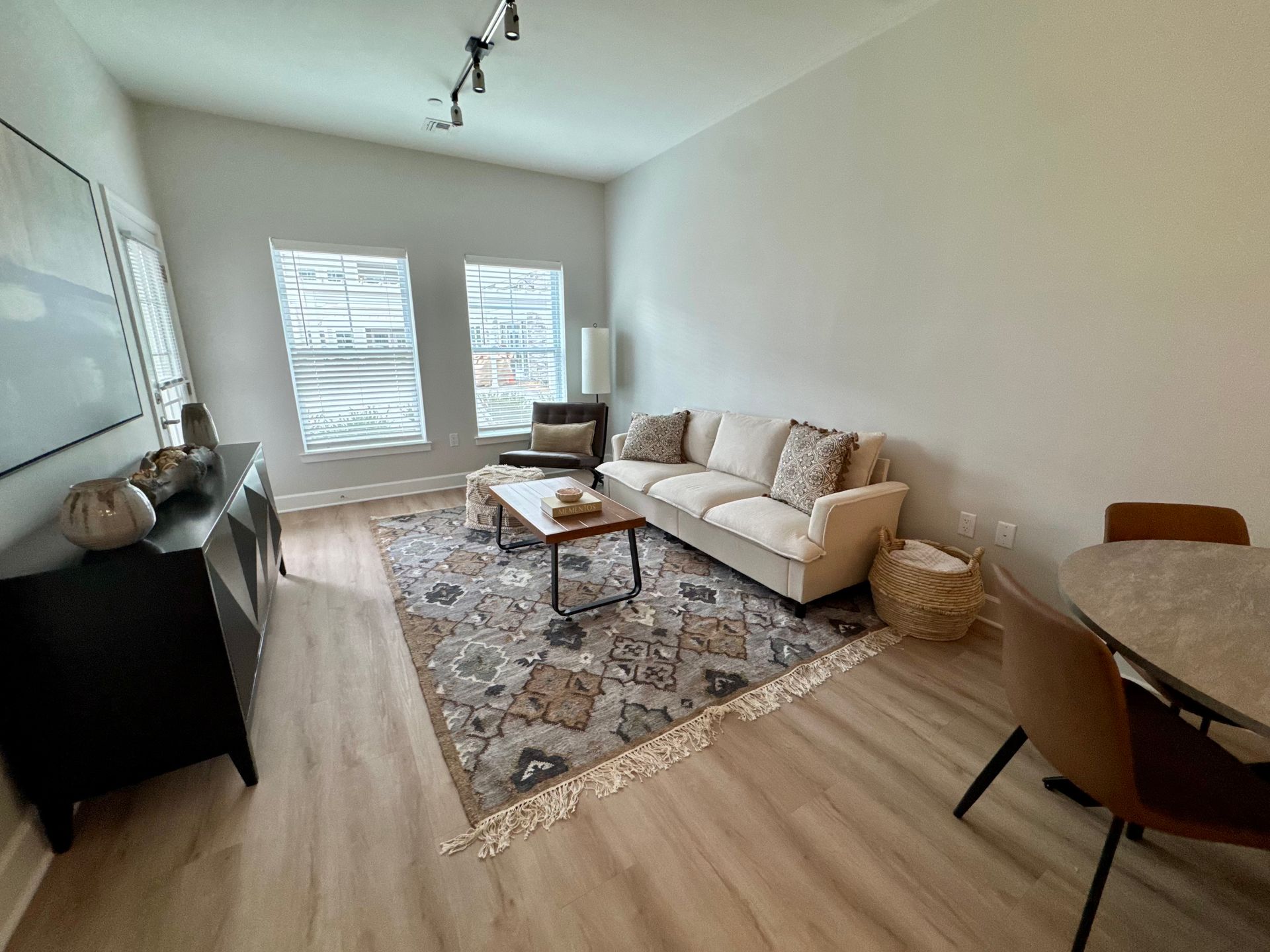 Bright living room with beige sofa, patterned rug, round table, and large windows.