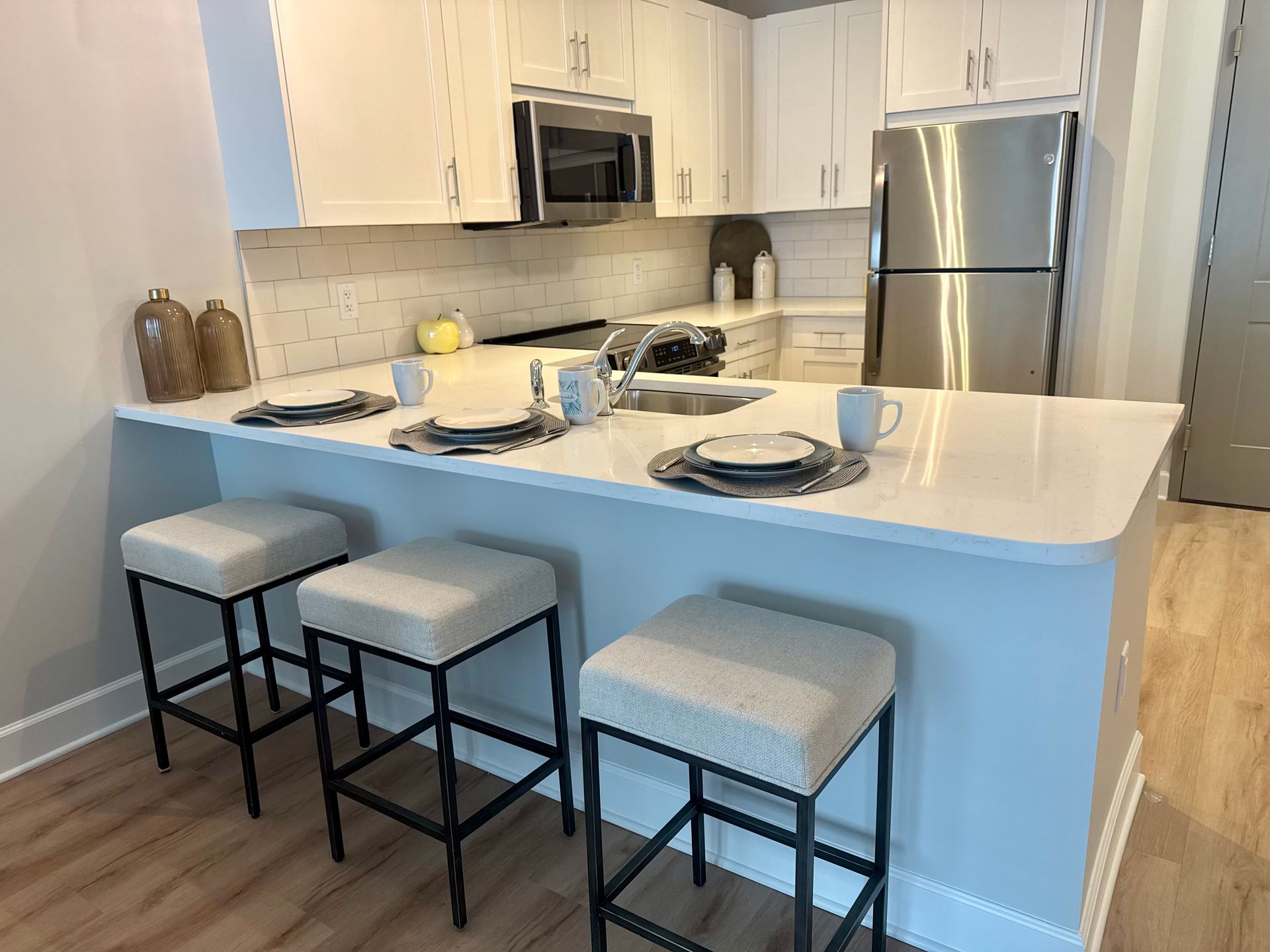 Modern white kitchen with stainless steel appliances, island, and three gray bar stools