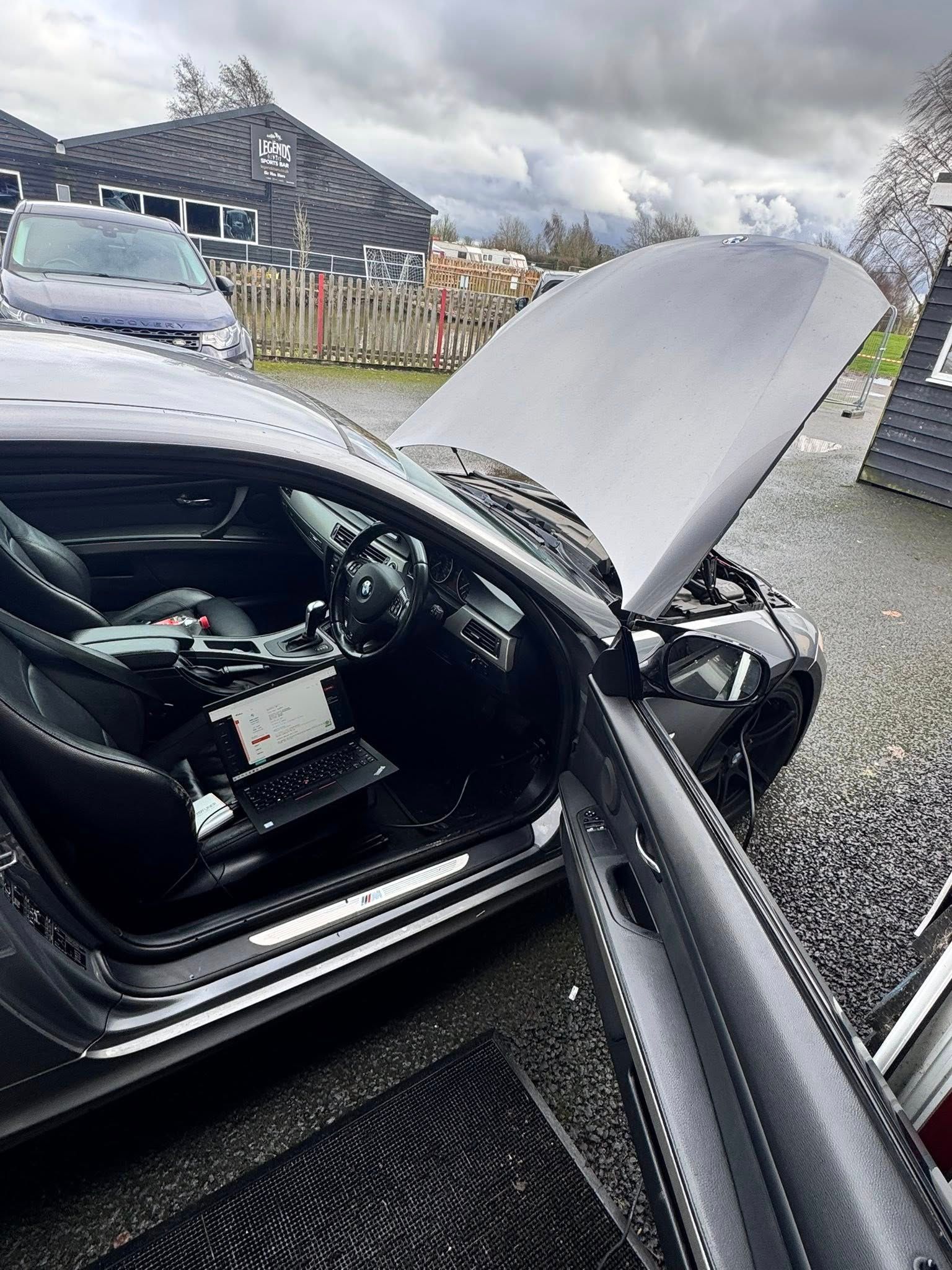 Black car with hood open, showing engine bay and damaged front end in a gravel driveway.