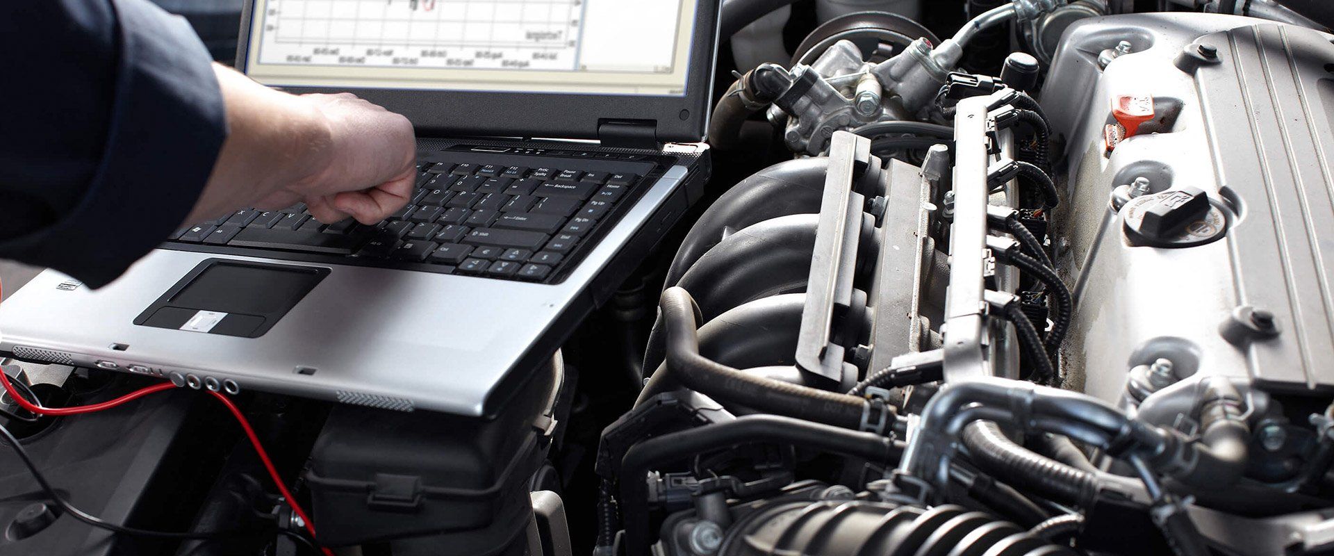 A hand uses a laptop to diagnose a car engine in an open engine bay.