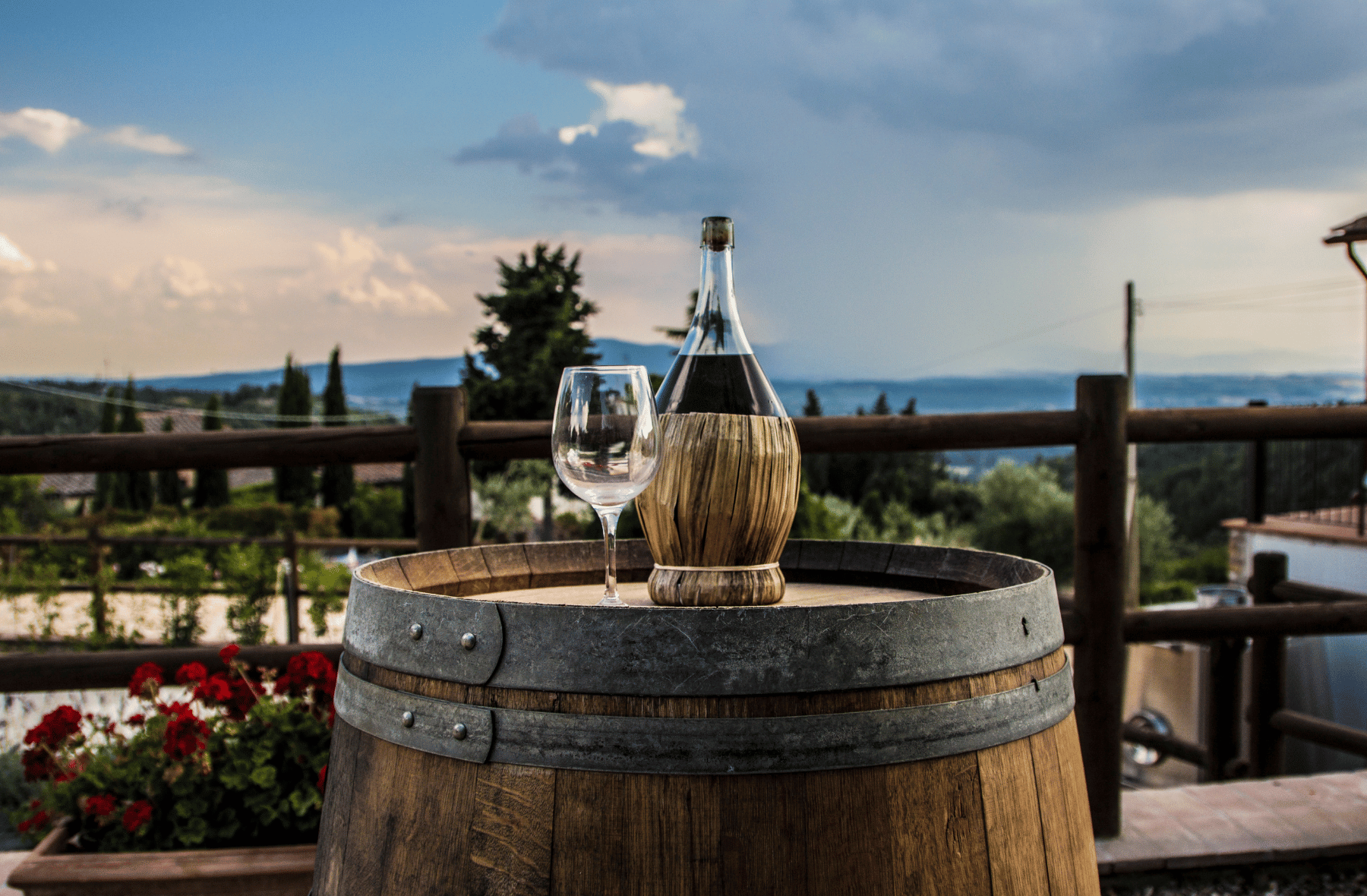 A bottle of wine and a glass of wine are on a wooden barrel.