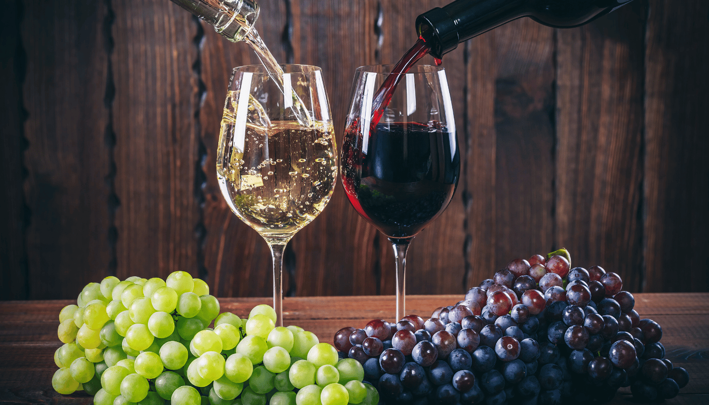 A bottle of wine is being poured into two glasses next to a bunch of grapes.