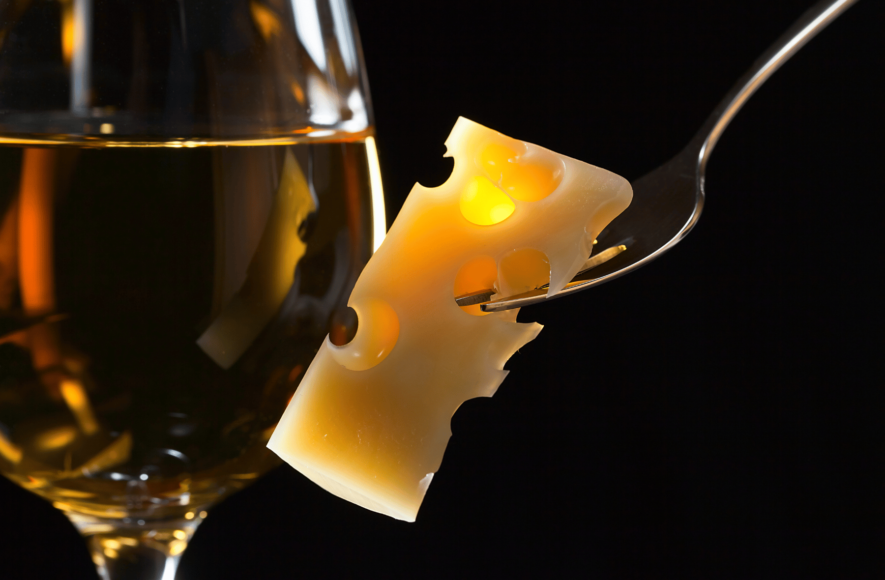 A slice of cheese on a fork next to a glass of wine