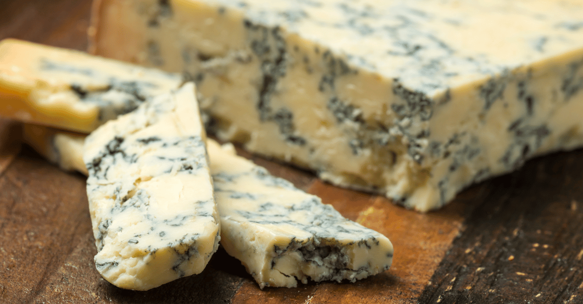 A piece of blue cheese is sitting on a wooden cutting board.