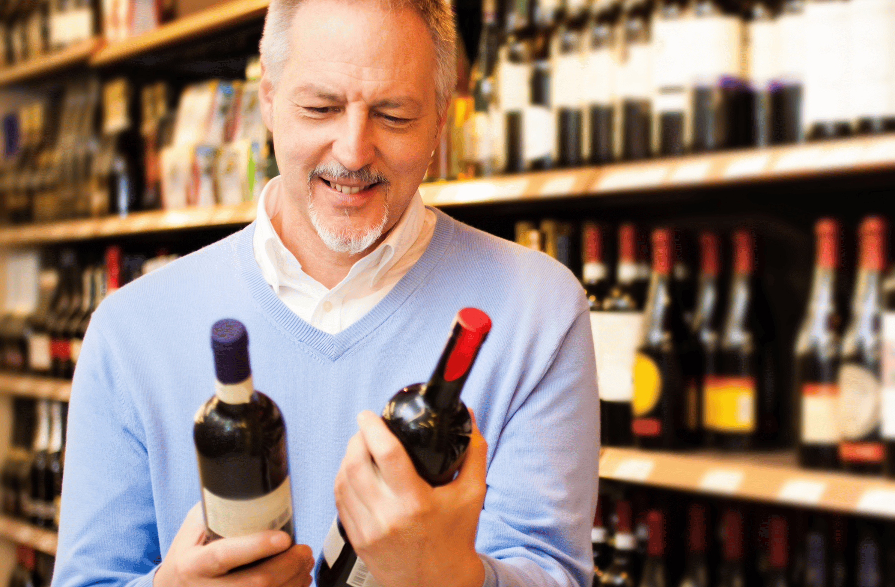 A man is holding two bottles of wine in a liquor store.