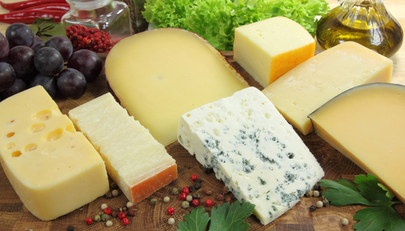 A variety of cheeses and grapes are on a wooden cutting board.