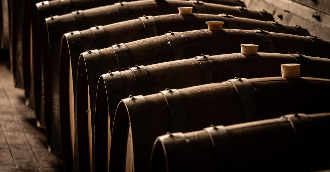 A row of wooden barrels are lined up in a dark room.