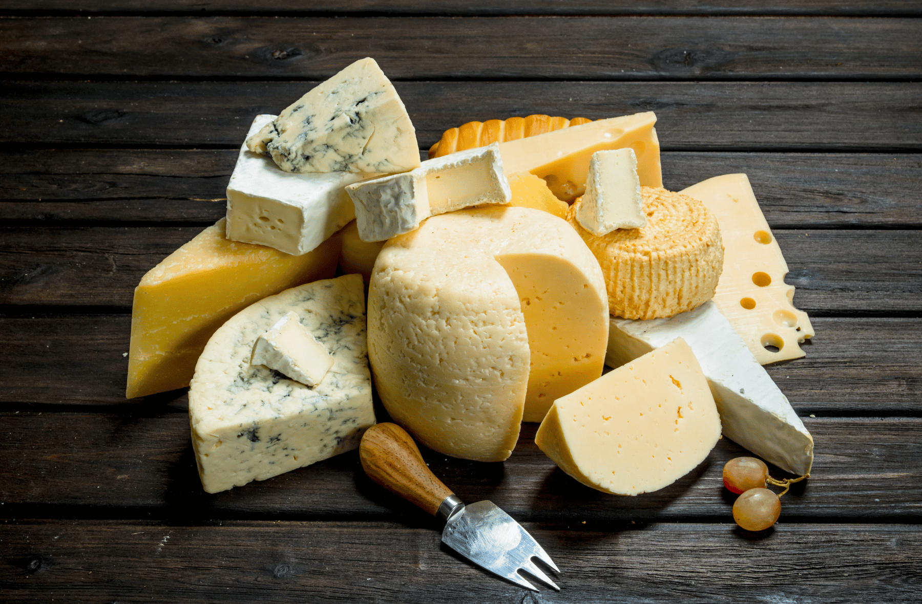 A variety of cheeses are stacked on top of each other on a wooden table.