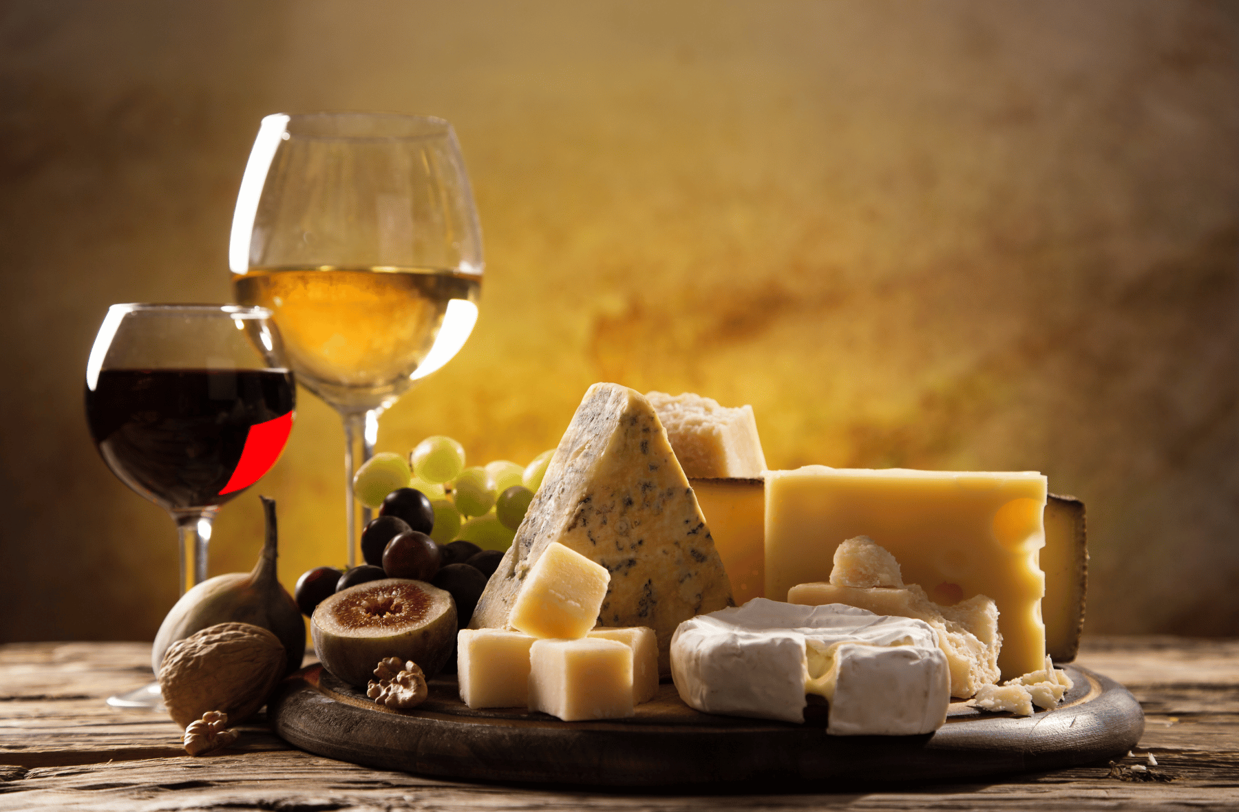 A wooden table topped with a variety of cheeses and a glass of wine.