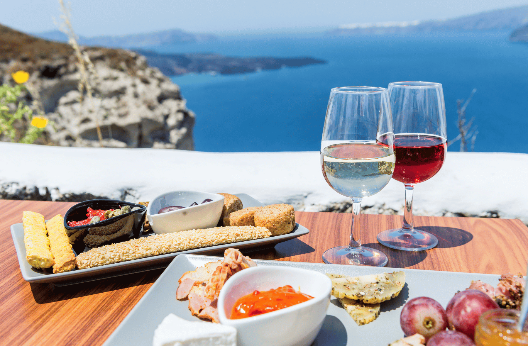 A plate of food and two glasses of wine on a table with a view of the ocean.