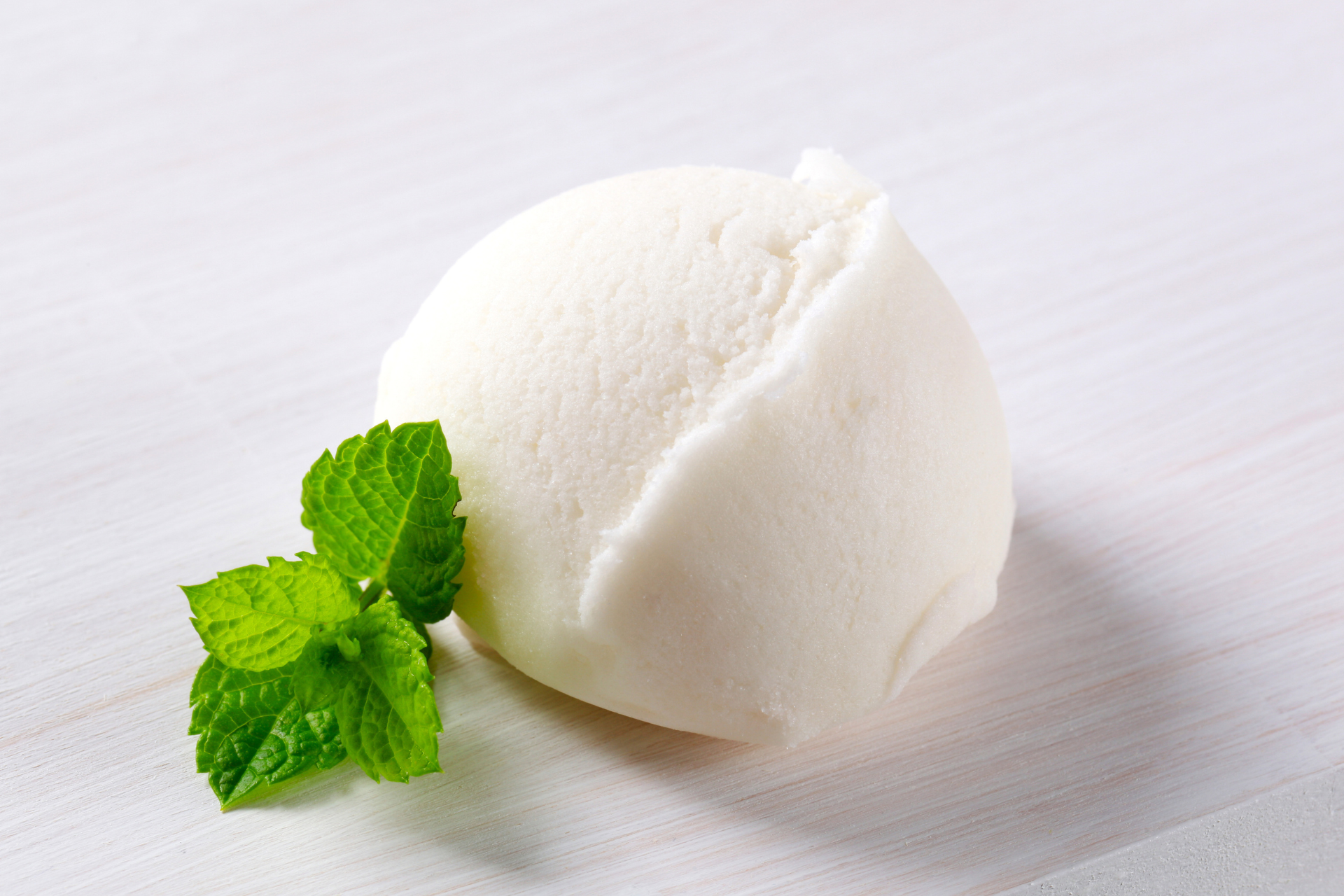 A scoop of ice cream with mint leaves on a white surface.