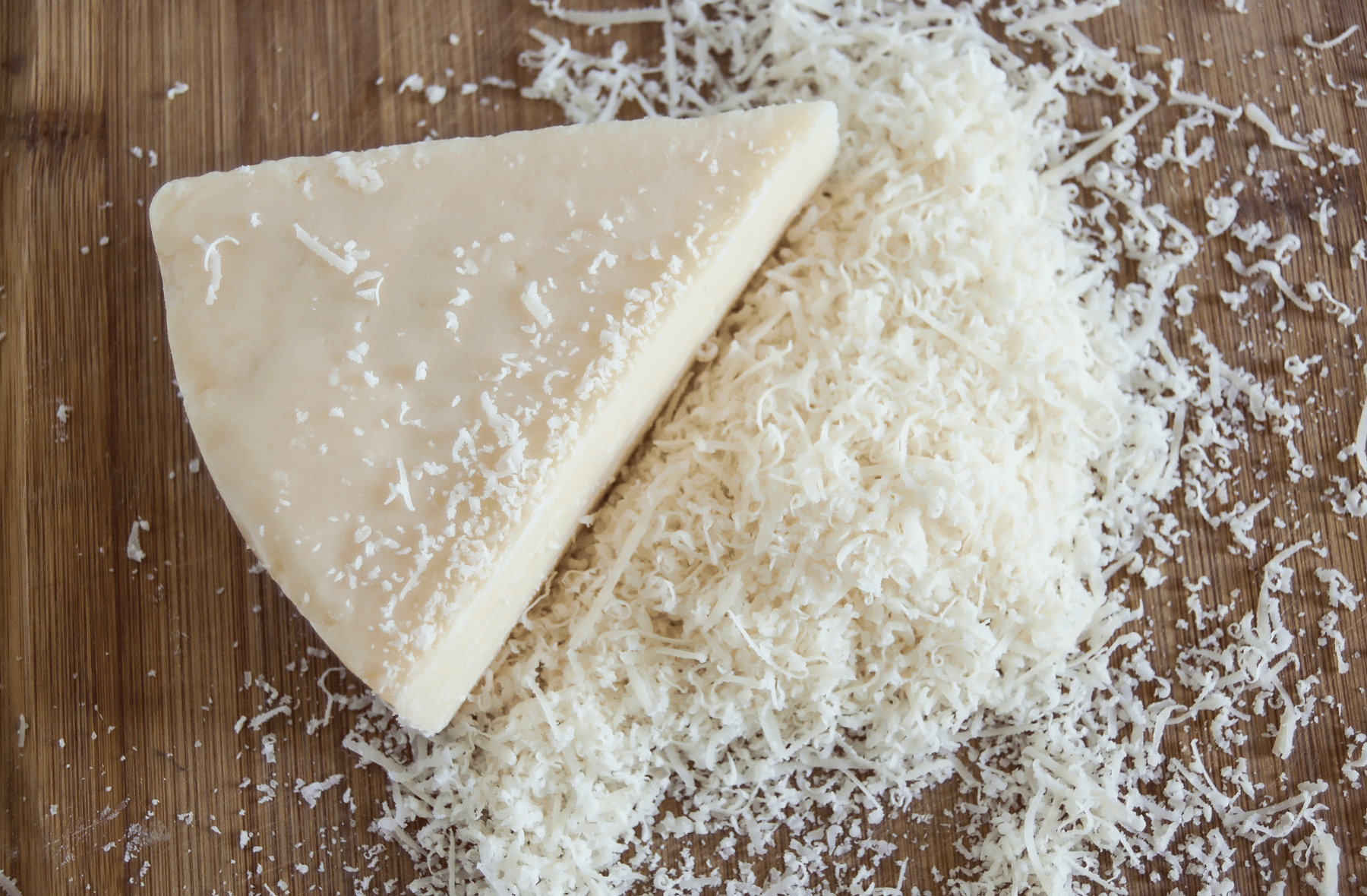 A piece of Parmesan cheese is sitting on top of a pile of shredded cheese.