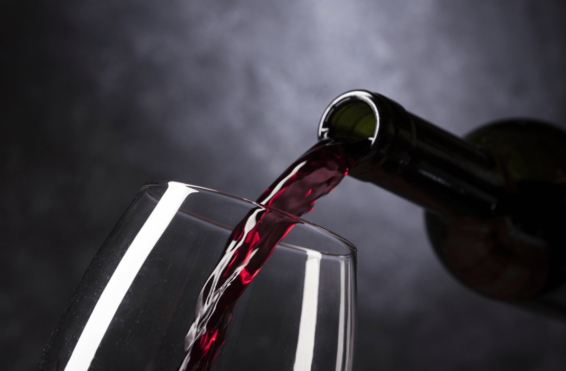 A bottle of red wine is being poured into a glass.