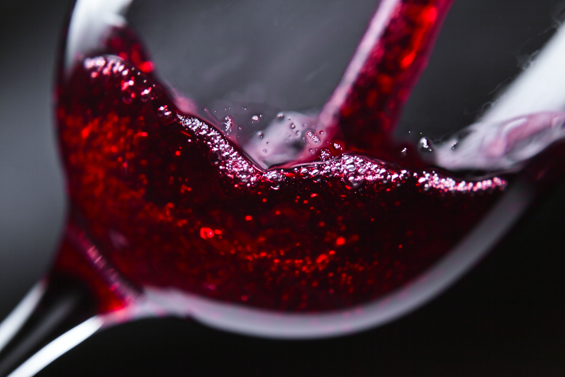 Red wine is being poured into a glass on a black background.