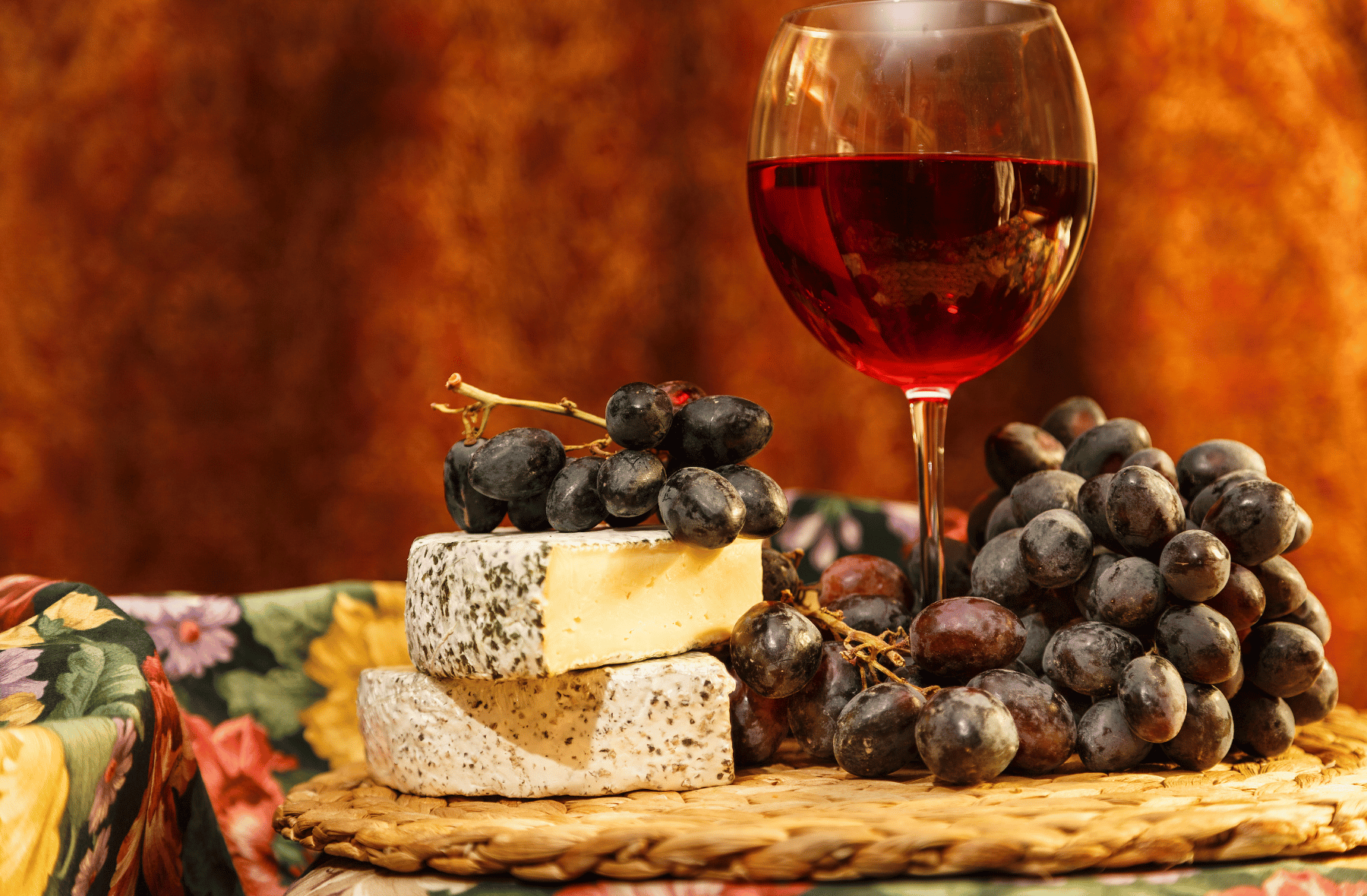 A glass of red wine next to a bunch of grapes and cheese