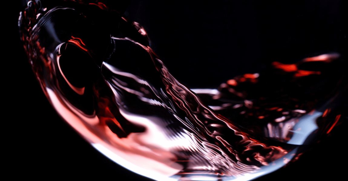 A glass of red wine is being poured into a glass on a black background.